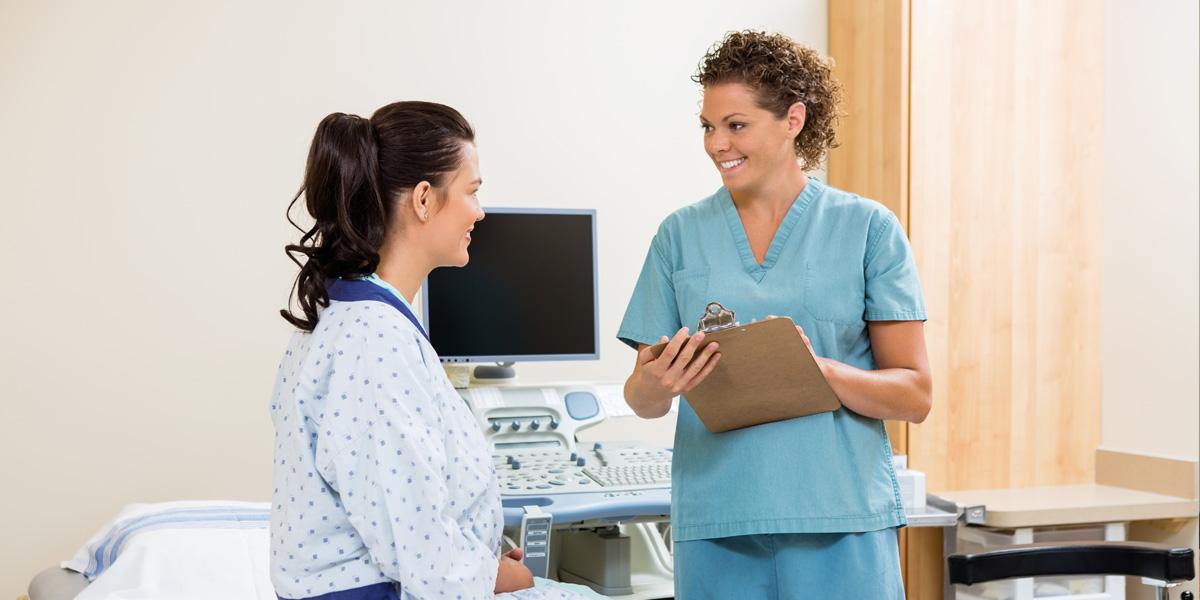 Health care worker talks with patient in hospital bed.